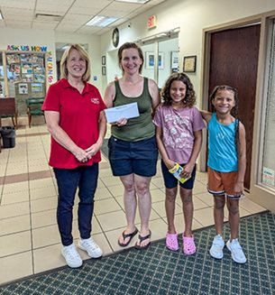 A BFCU representative standing with the recipient of the Homebuyer Challenge reward and her two daughters